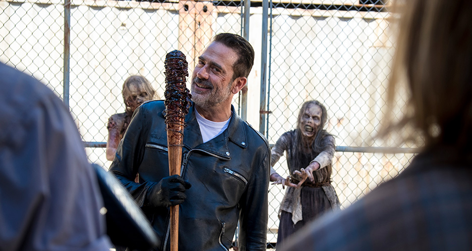 Man in leather jacket holding baseball bat is surrounded by zombies.